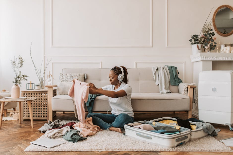 A woman with braided hair packs a suitcase at home while listening to music on headphones.